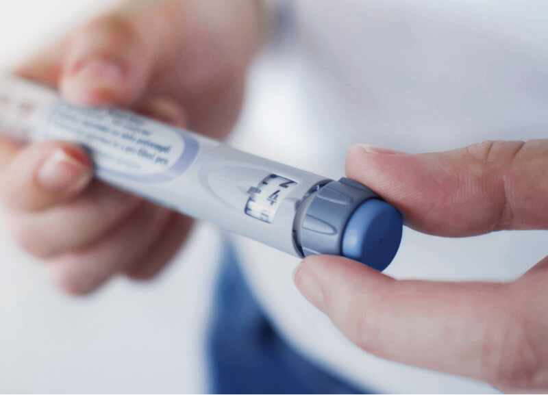 Hands adjusting the dose selector on an injection pen, showing the dosage window and rotating dial.