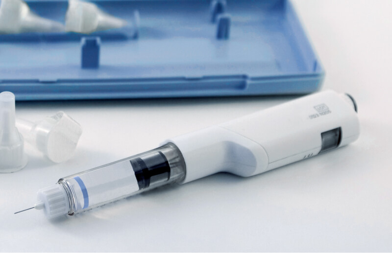 Disposable injection pen device lying on a clean surface, with needle attached and protective caps visible nearby.