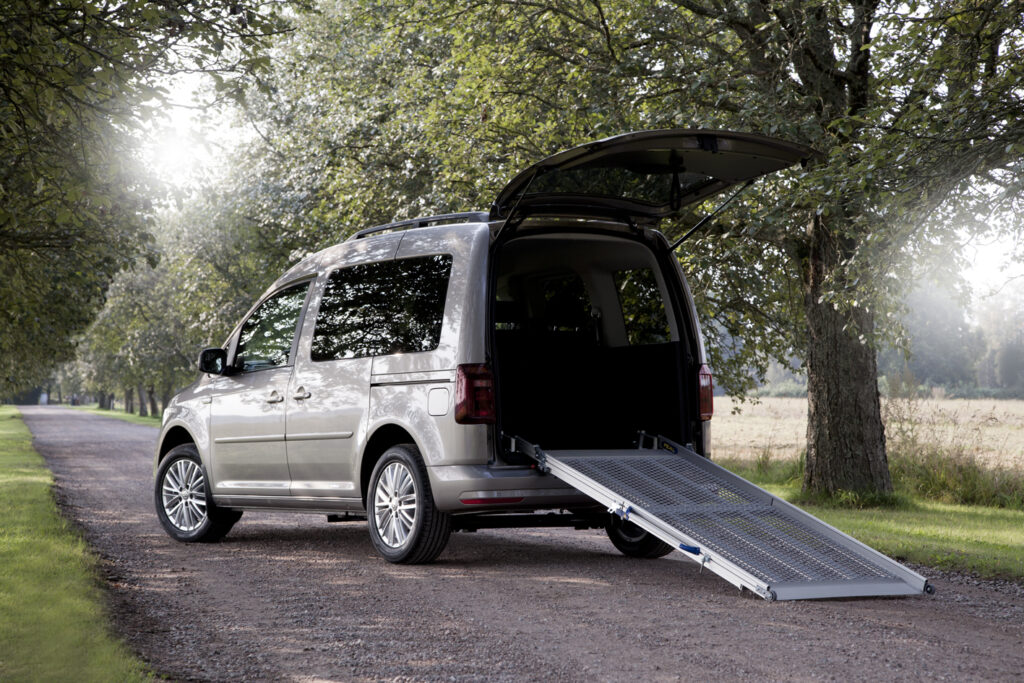 a van standing in a greenery setting with open back door and a ramp for wheelchair users