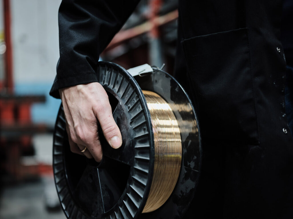 A close up shot of a hand carrying a reel of high quality copper wire for spring manufacturing.