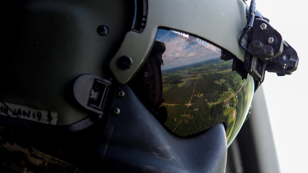 A close up shot of a pilot in the defense sector wearing a dark green helmet with built in googles.
