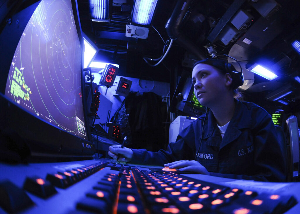 A female sailor at the navigation centre of a defense ship, assessing conditions.