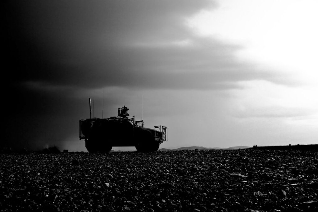 A defense vehicle driving on rubble in a sepia photograph with a dark stormy sky.