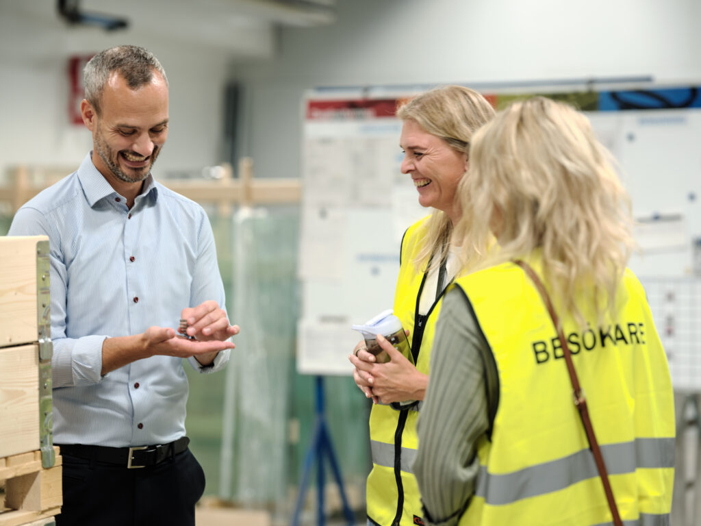 Three Lesjofors employees inspecting a small spring, two females in yellow high visibility jackets and one male in a blue shirt.
